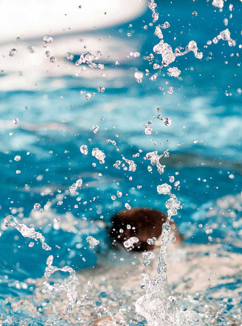 Water droplets caught mid-air from a splash in a clear pool.