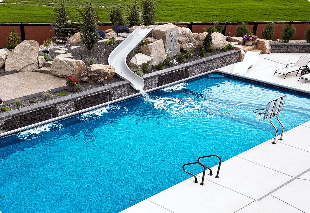 Custom vinyl liner inground pool with waterfalls, slide, tanning ledge, autocover, and basketball net.