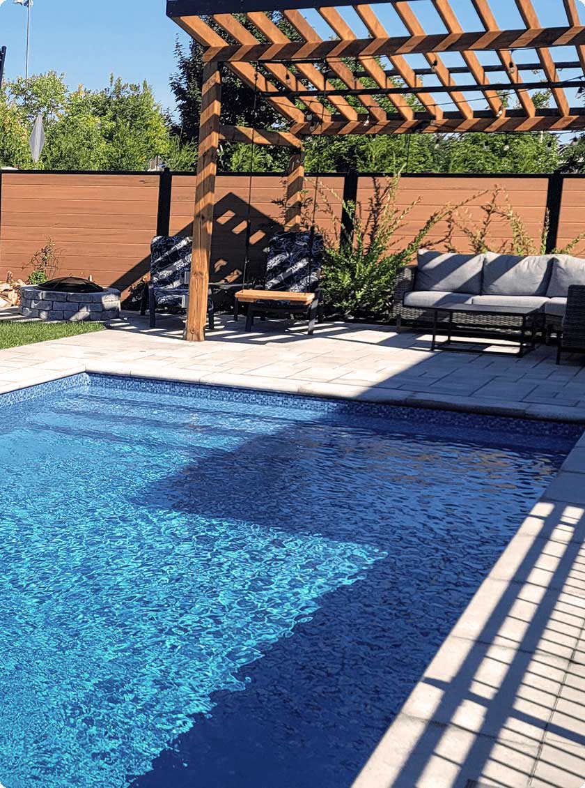 Vinyl pool with stone edging and galvanized steel panel structure behind landscaping.