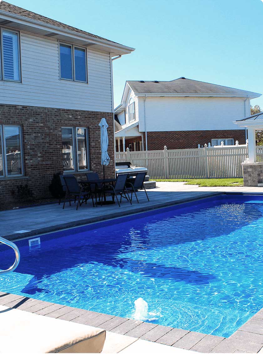 Vinyl liner pool bordered by polymer walls, set in a sunny backyard with stone pavers.