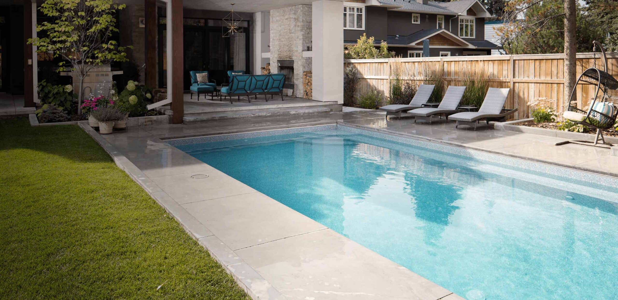 Long rectangular vinyl pool beside a covered outdoor lounge and manicured lawn.