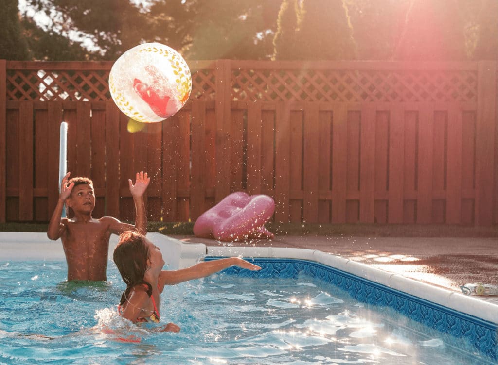 Kids splashing with colorful beach balls in a backyard vinyl liner pool.