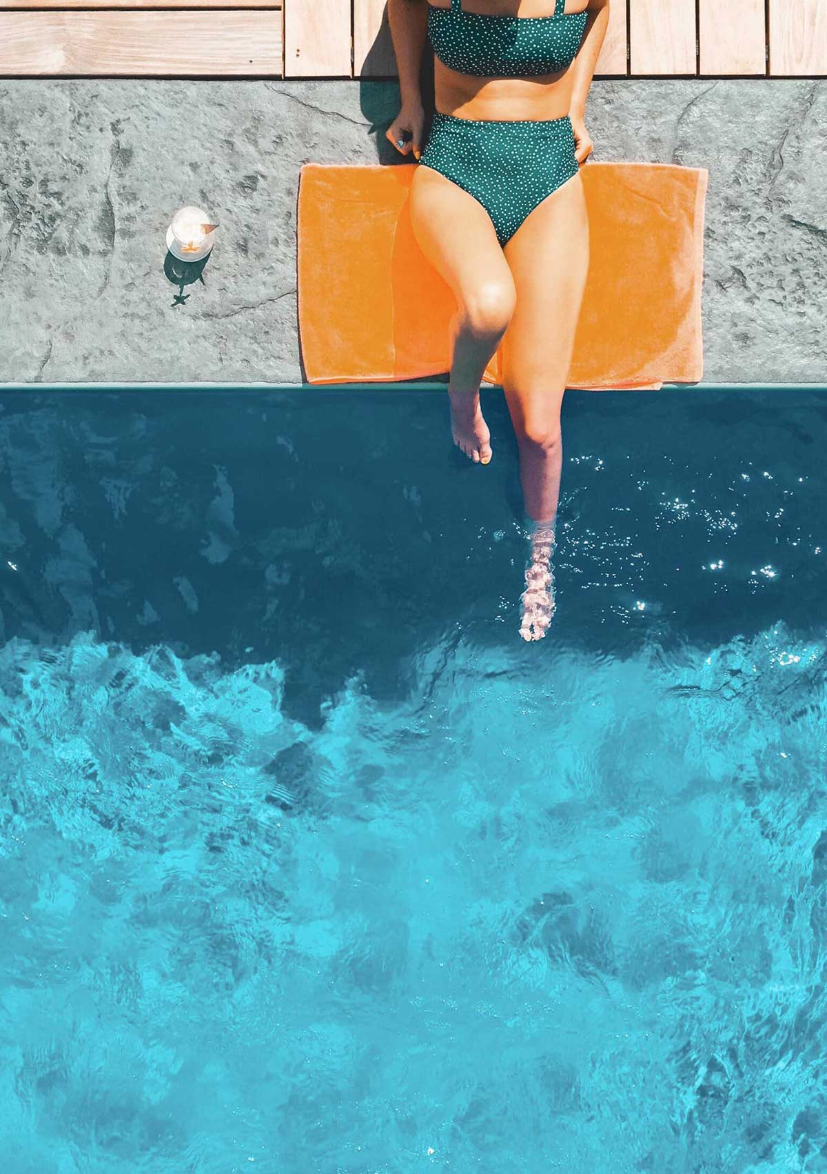 woman lounging poolside on orange blanket with feet in water